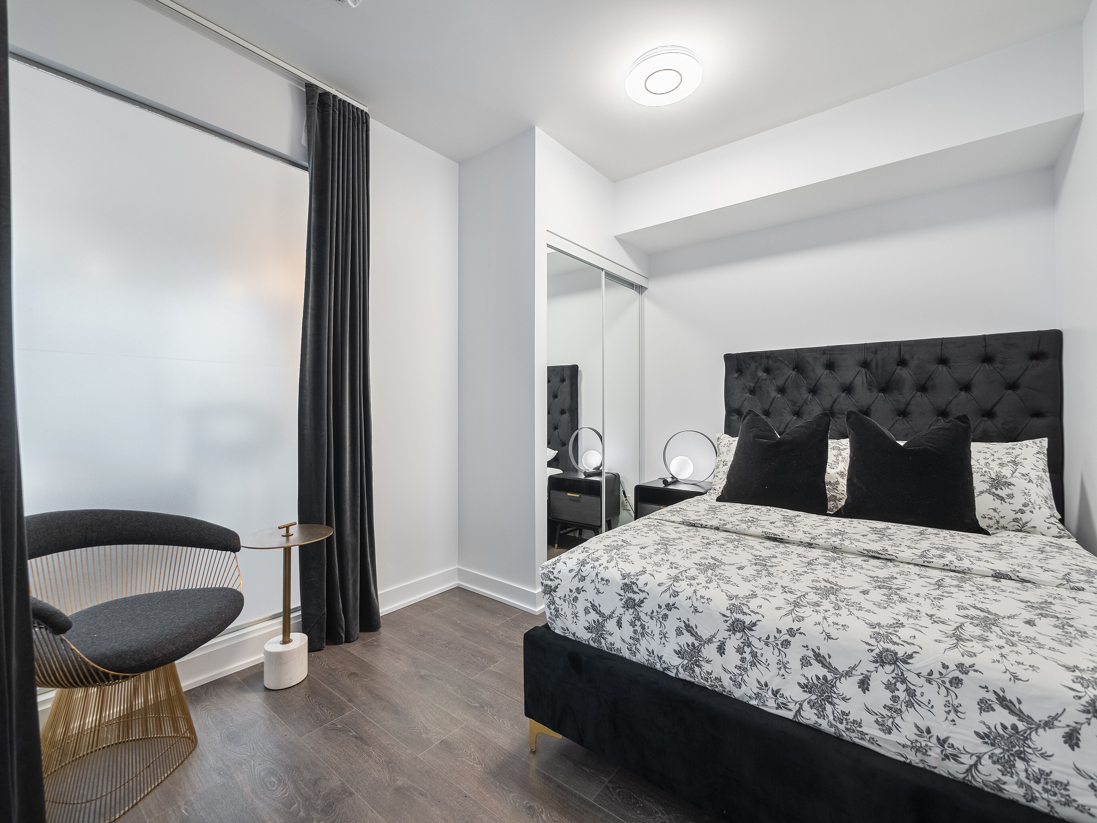 Quarto moderno com uma cama grande, uma cadeira, mesa de cabeceira e um espelho.