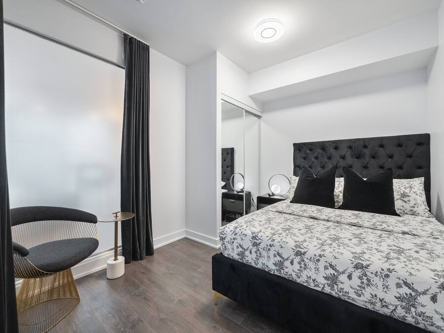 A modern bedroom with a large bed, a chair, a bedside table, and a mirror.