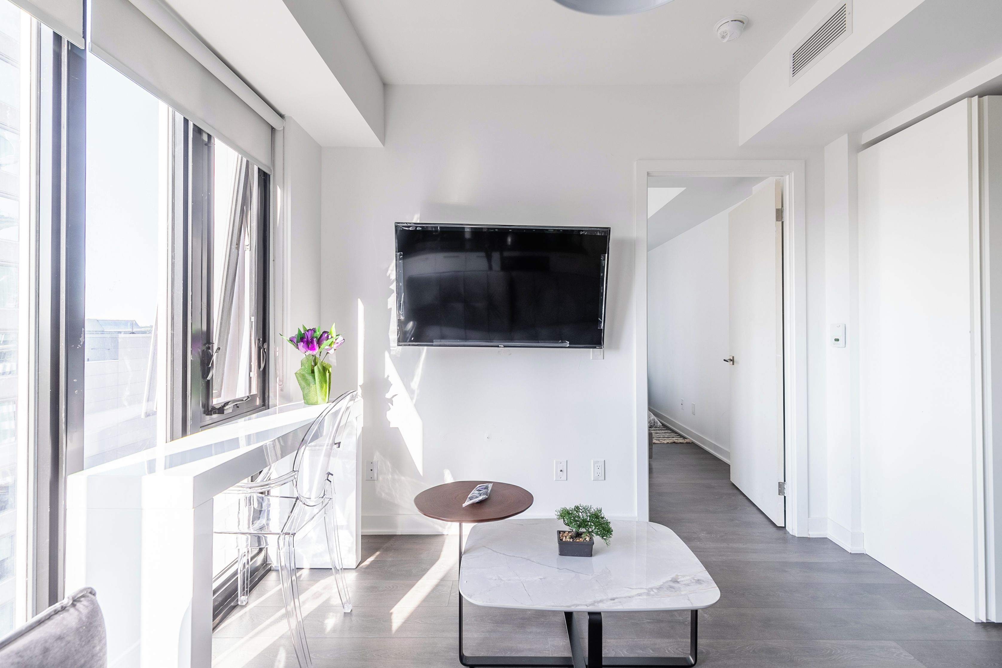 Une chambre d’hôtel moderne dotée d’une grande fenêtre, d’un téléviseur à écran plat fixé au mur, d’une petite table ronde agrémentée d’une plante, et offrant une vue sur la ville.