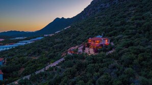 A hillside house with a red roof, surrounded by dense vegetation and mountains in the background. - ISTLADA TAS EV APART (Demre)