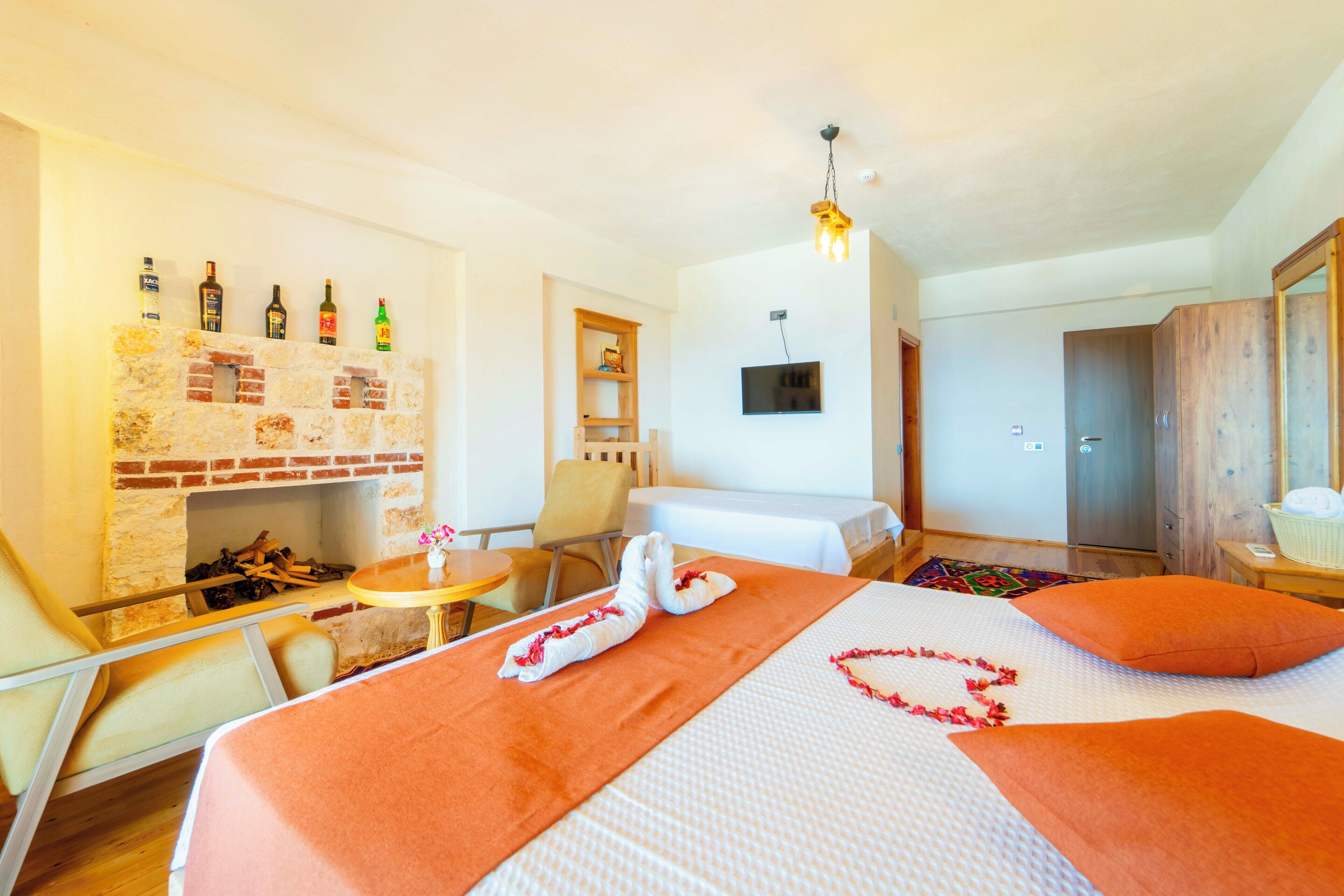 A hotel room with a brick wall, a fireplace, a TV, a bed with orange bedding, and a small table with a chair.