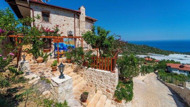 A stone building with a view of the sea, a sign reading 'ISTALADA,' and a paved area with potted plants. - ISTLADA TAS EV APART (Demre)