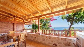 A wooden deck with a table and chairs, a stone wall, and a view of the sea. - ISTLADA TAS EV APART (Demre)