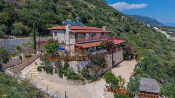 Villa en una ladera con techo de tejas rojas, paneles solares y fachada de piedra.