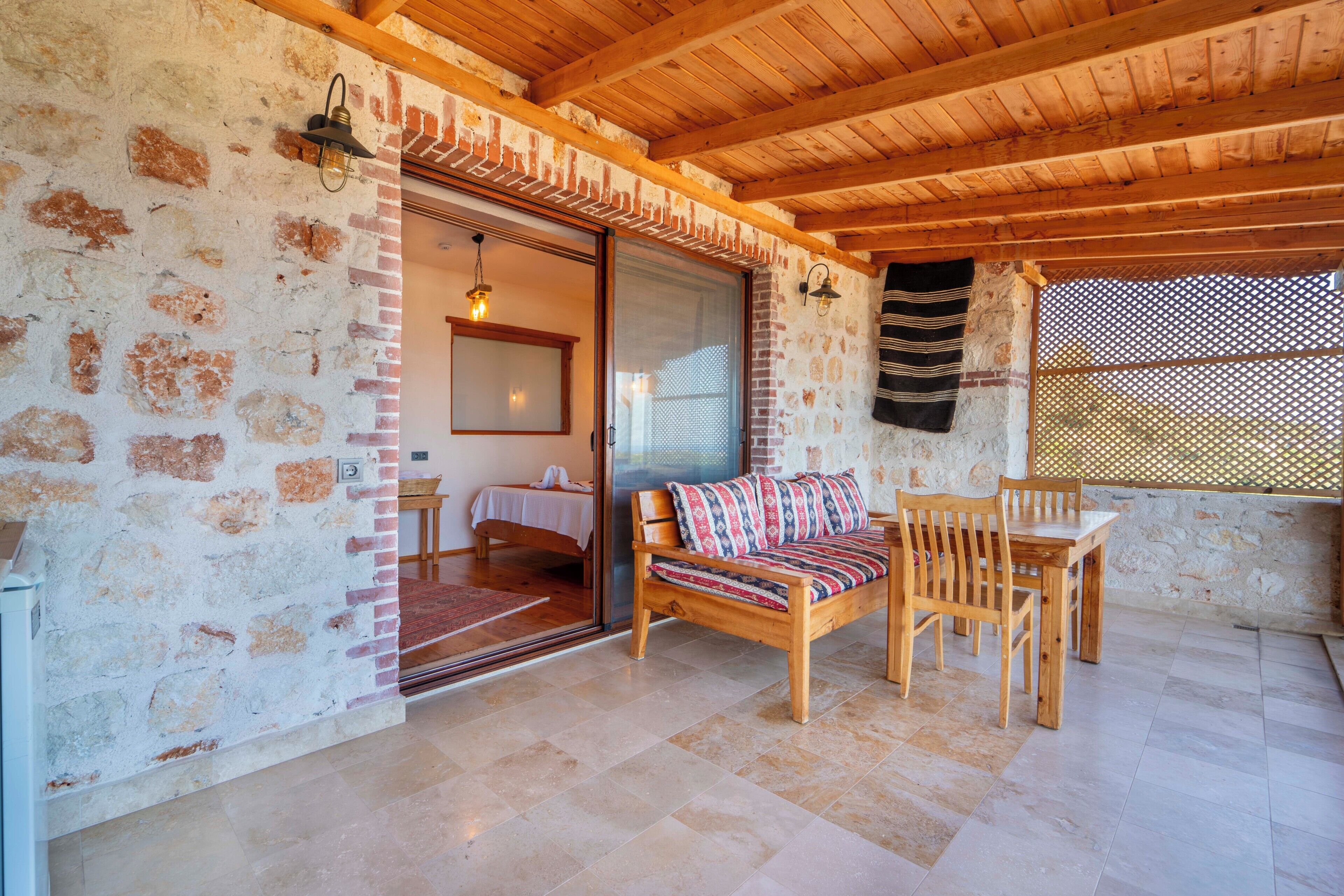 A room with a wooden ceiling, stone walls, a bed, a sofa, and a dining table.
