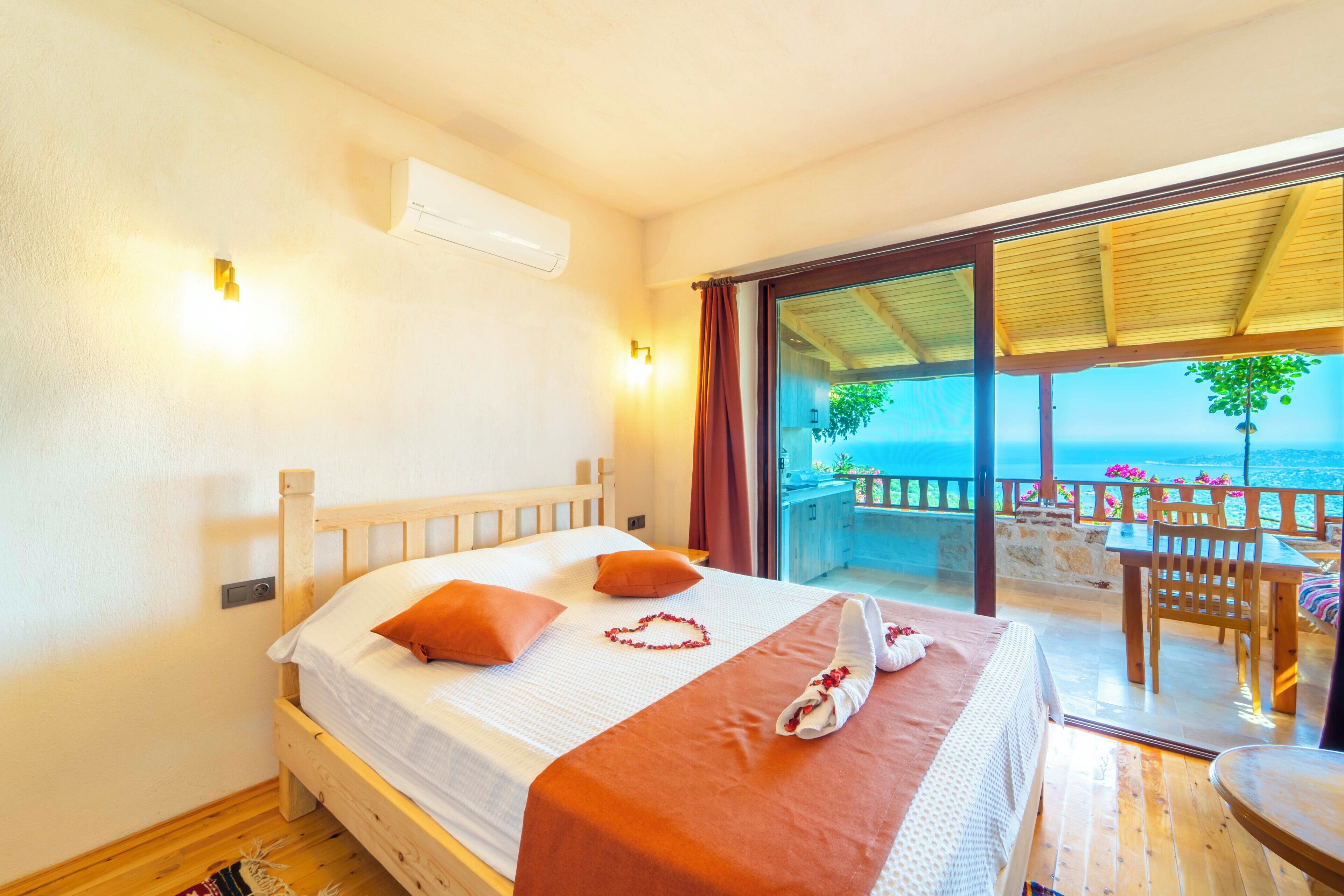 A bedroom with a bed, a nightstand, a window with a view of the sea, and a balcony with a table and chairs.