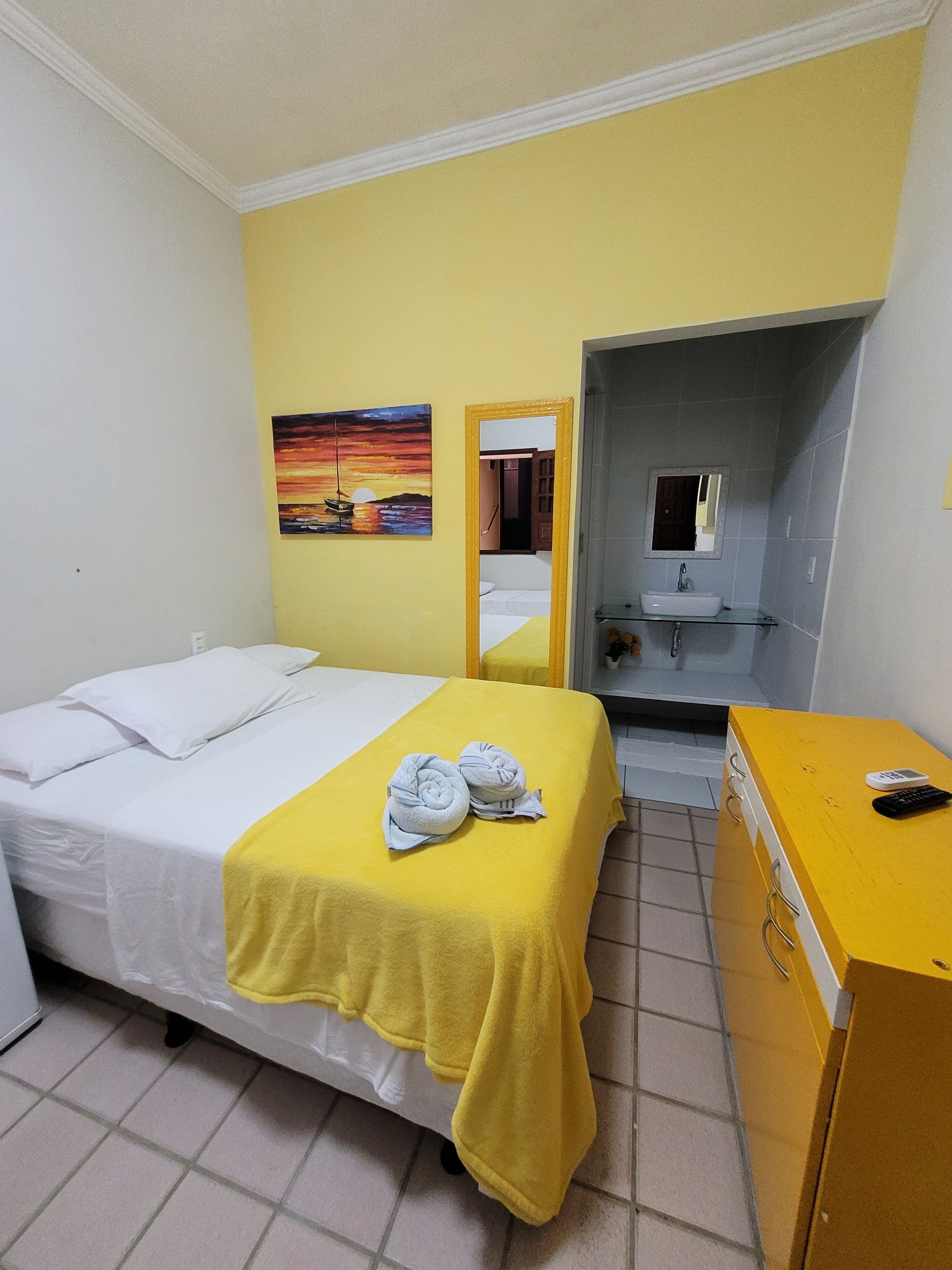 Una habitación de hotel con una cama, una toalla amarilla, un lavabo y un espejo.