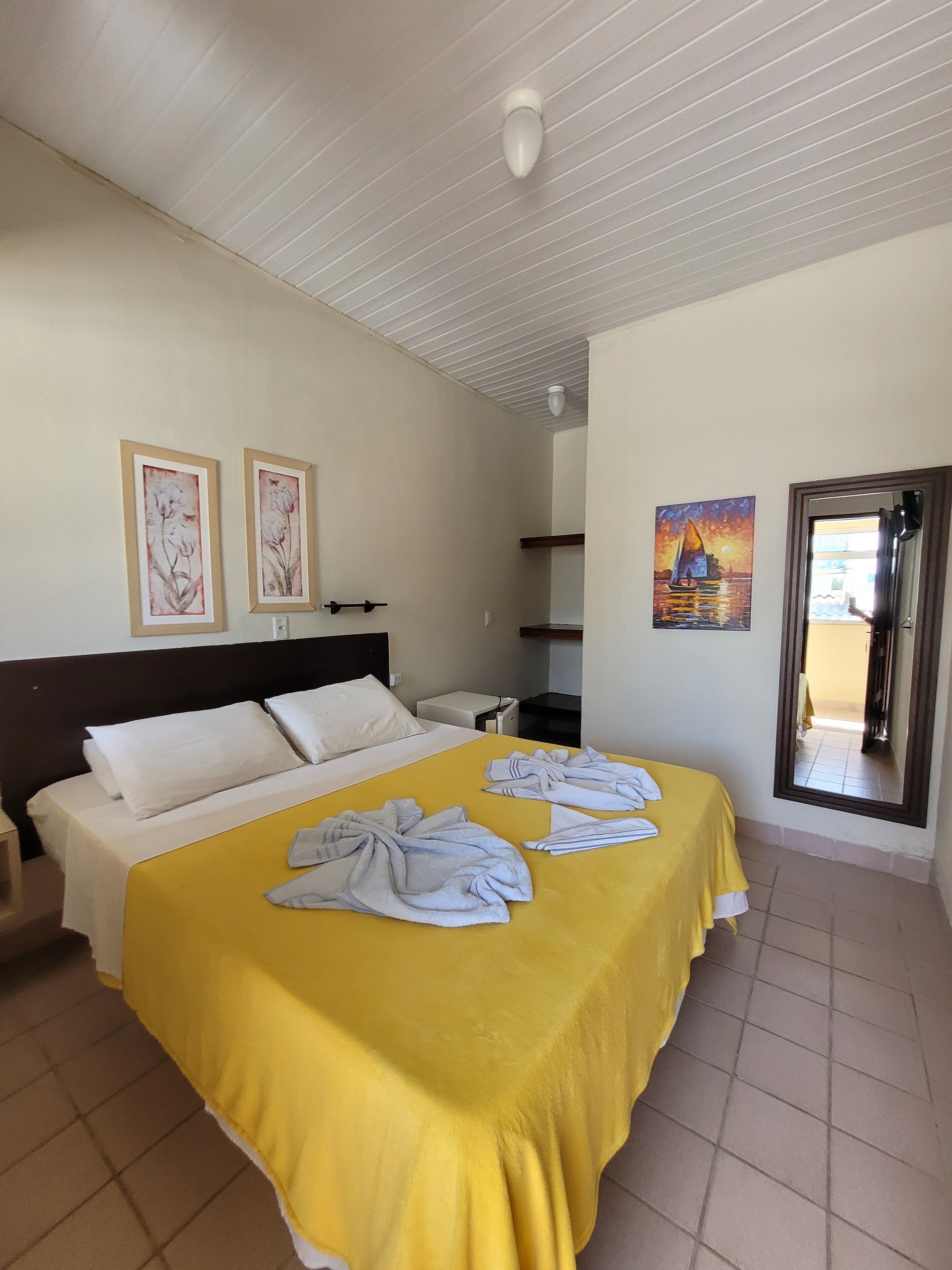Ein Hotelzimmer mit einem Bett, einem Nachttisch, einem Gemälde und einer Tür zu einem anderen Raum.