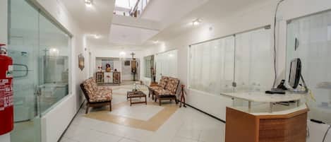 Un'ampia hall con una reception, poltrone a fantasia, un lampadario e un estintore.