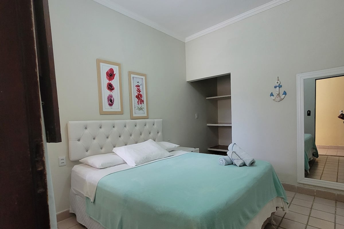 Une chambre bien rangée, avec un lit, une table de chevet, un miroir et une étagère.