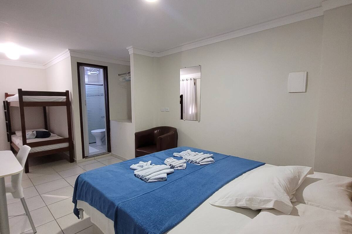 Une chambre d’hôtel avec un lit, un bureau, une chaise et une salle de bain visible à travers une porte ouverte.