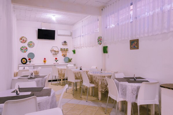 Un comedor con mesas y sillas, un televisor de pantalla plana, platos decorativos y un aire acondicionado instalado en la pared.