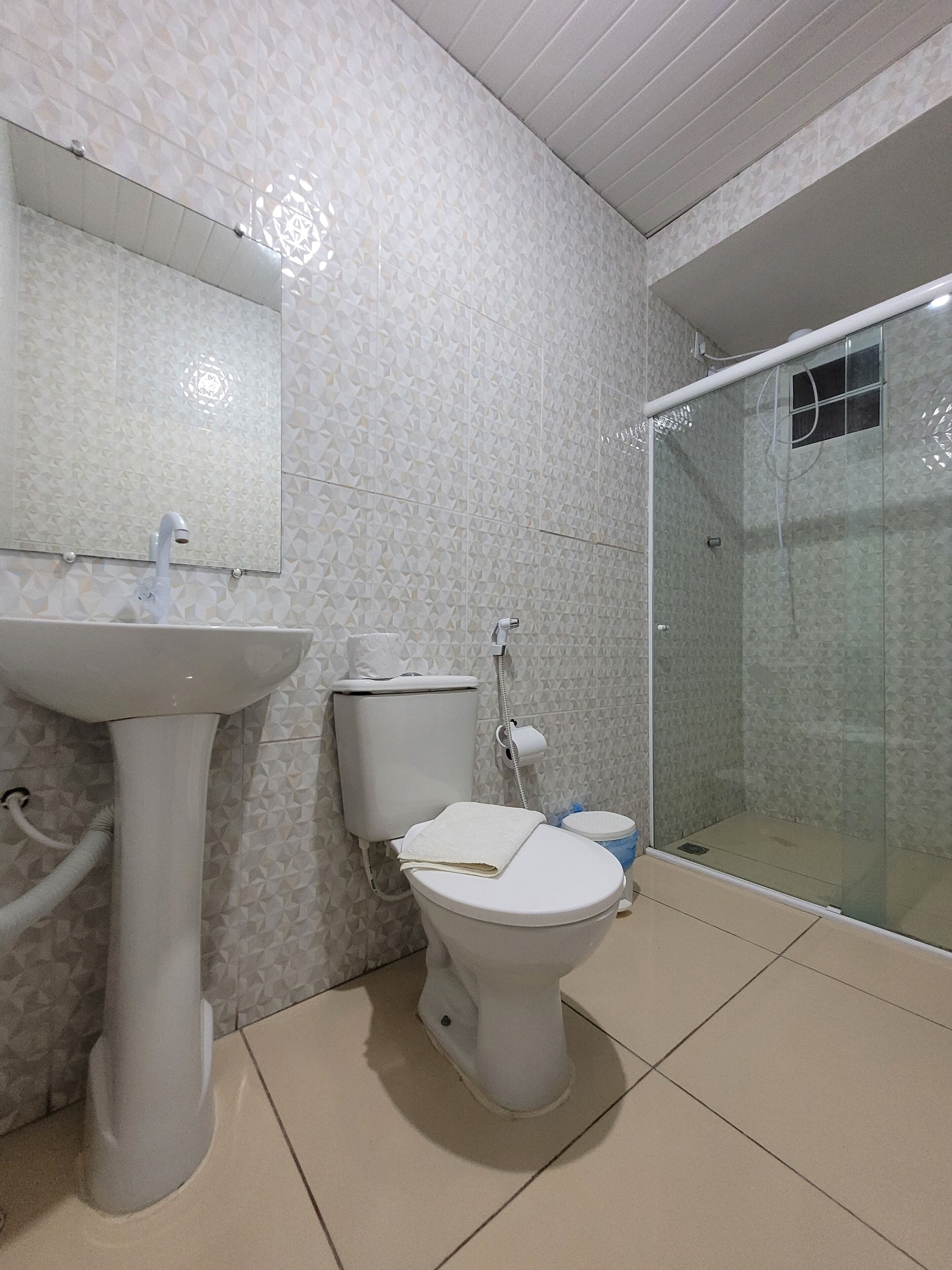 Baño con inodoro, lavamanos y ducha con mampara de vidrio.