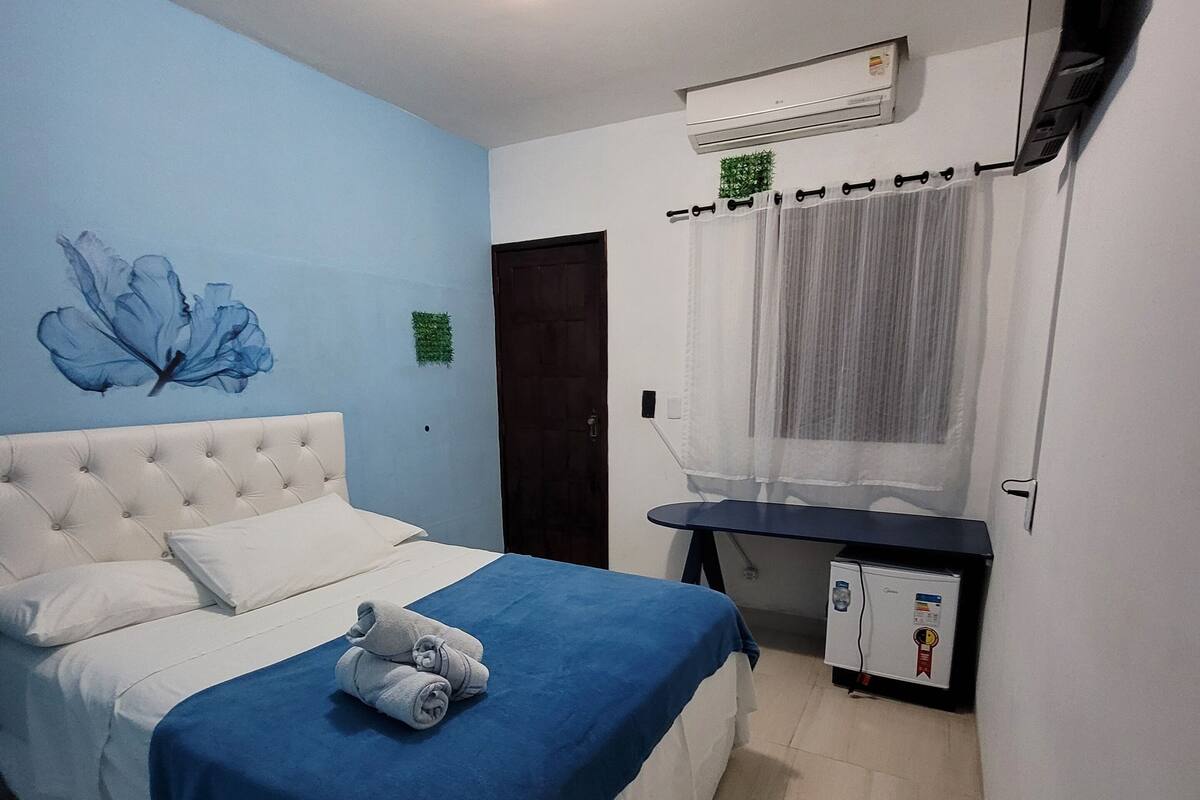 Une chambre avec un lit, un téléviseur à écran plat, un climatiseur et une petite table avec un réfrigérateur.