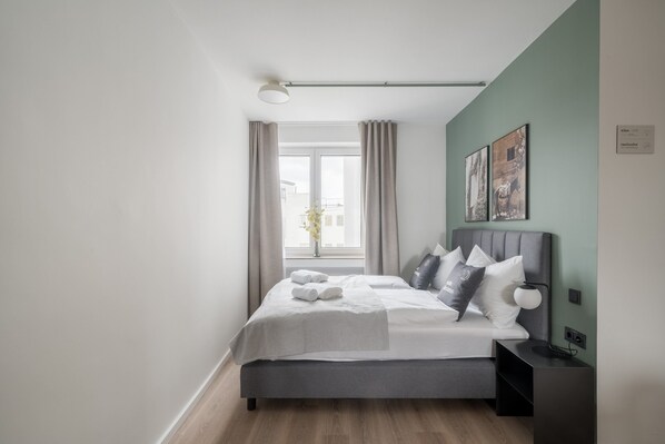 A modern bedroom with a bed, bedside table, and a window with curtains. - Limehome Saarbrücken Berliner Promenade (Saarbrücken)