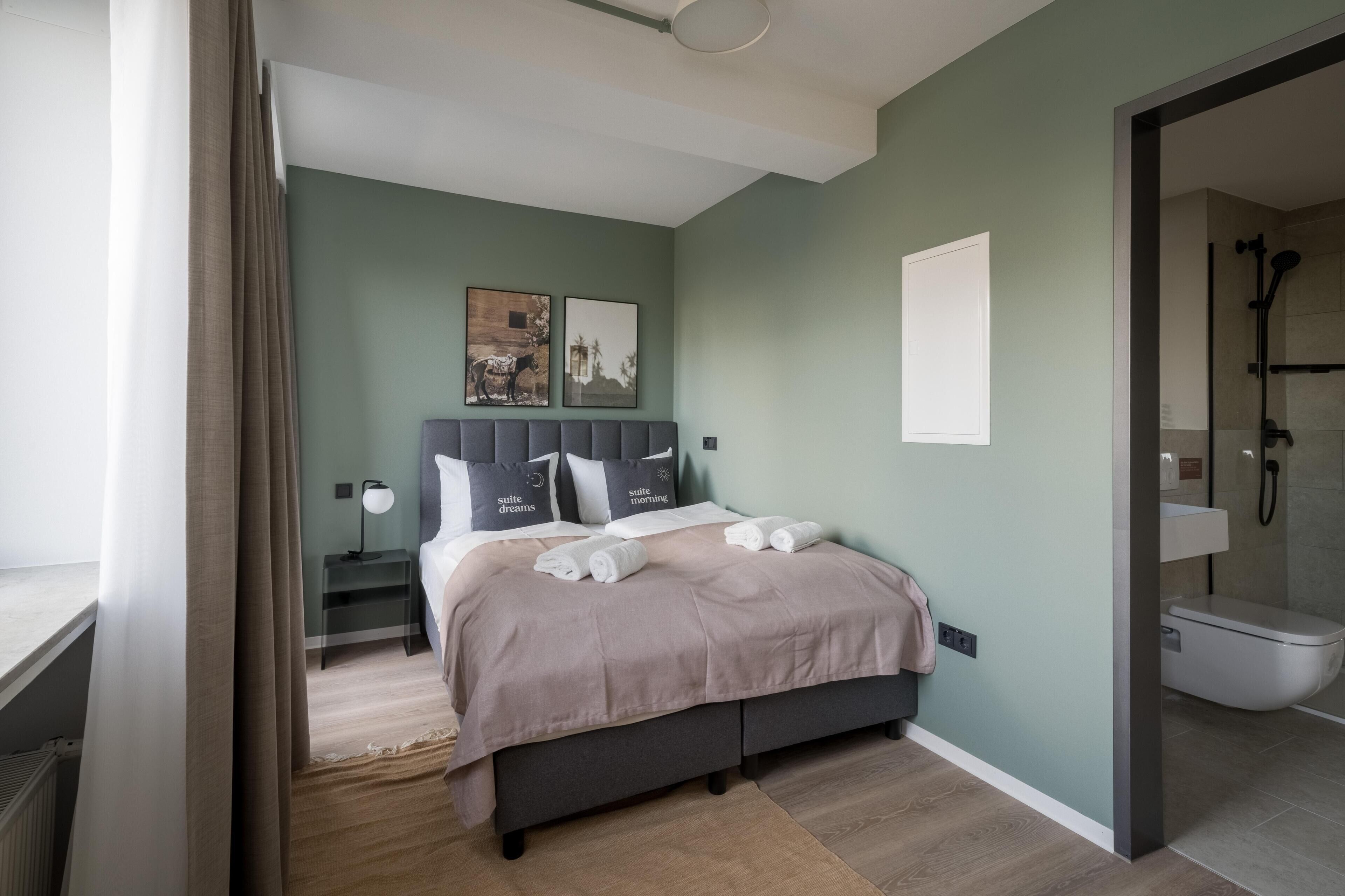 A modern bedroom with a bed, bedside tables, and a view into the bathroom.