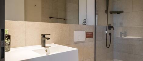 Un baño moderno con lavamanos blanco, inodoro y zona de ducha con cerramiento de vidrio.