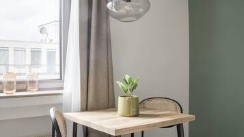 Un comedor con una mesa, sillas, una lámpara colgante, una planta en maceta y vistas al exterior a través de una ventana con cortinas.
