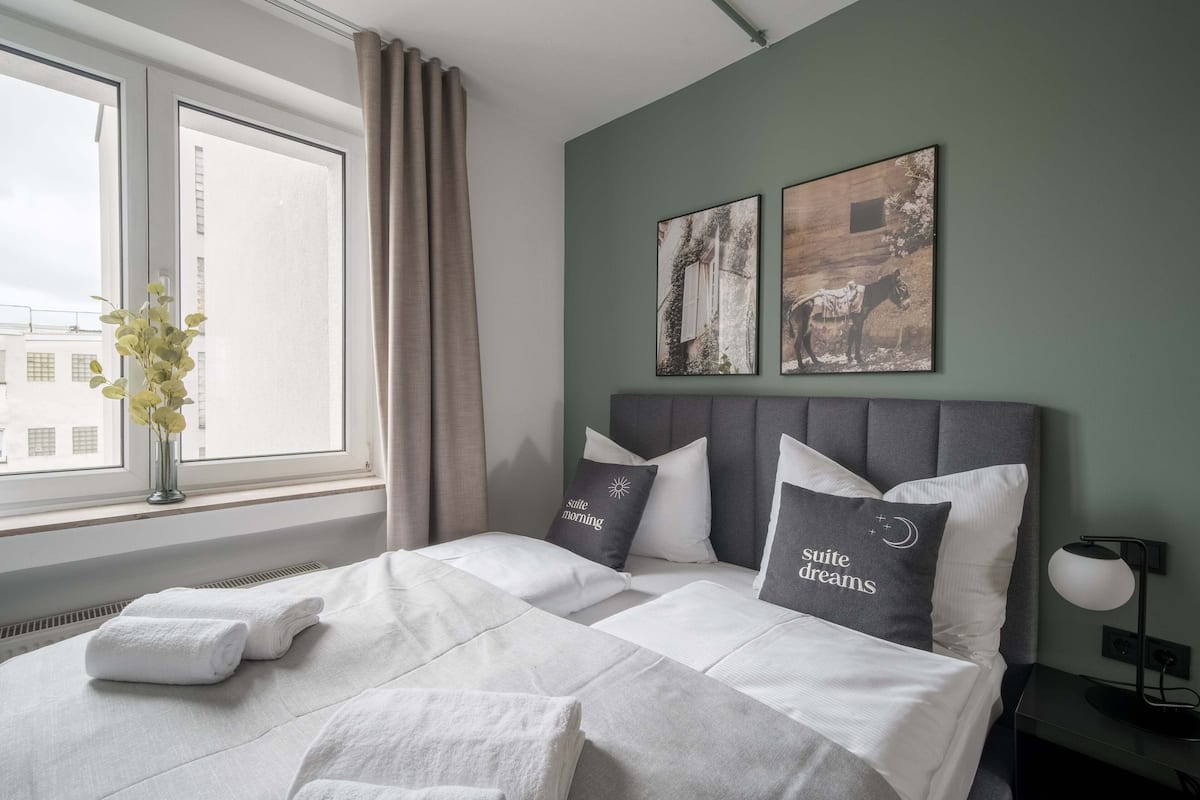 A neatly made bed with white linens and two pillows, a bedside lamp, and artwork on the wall.