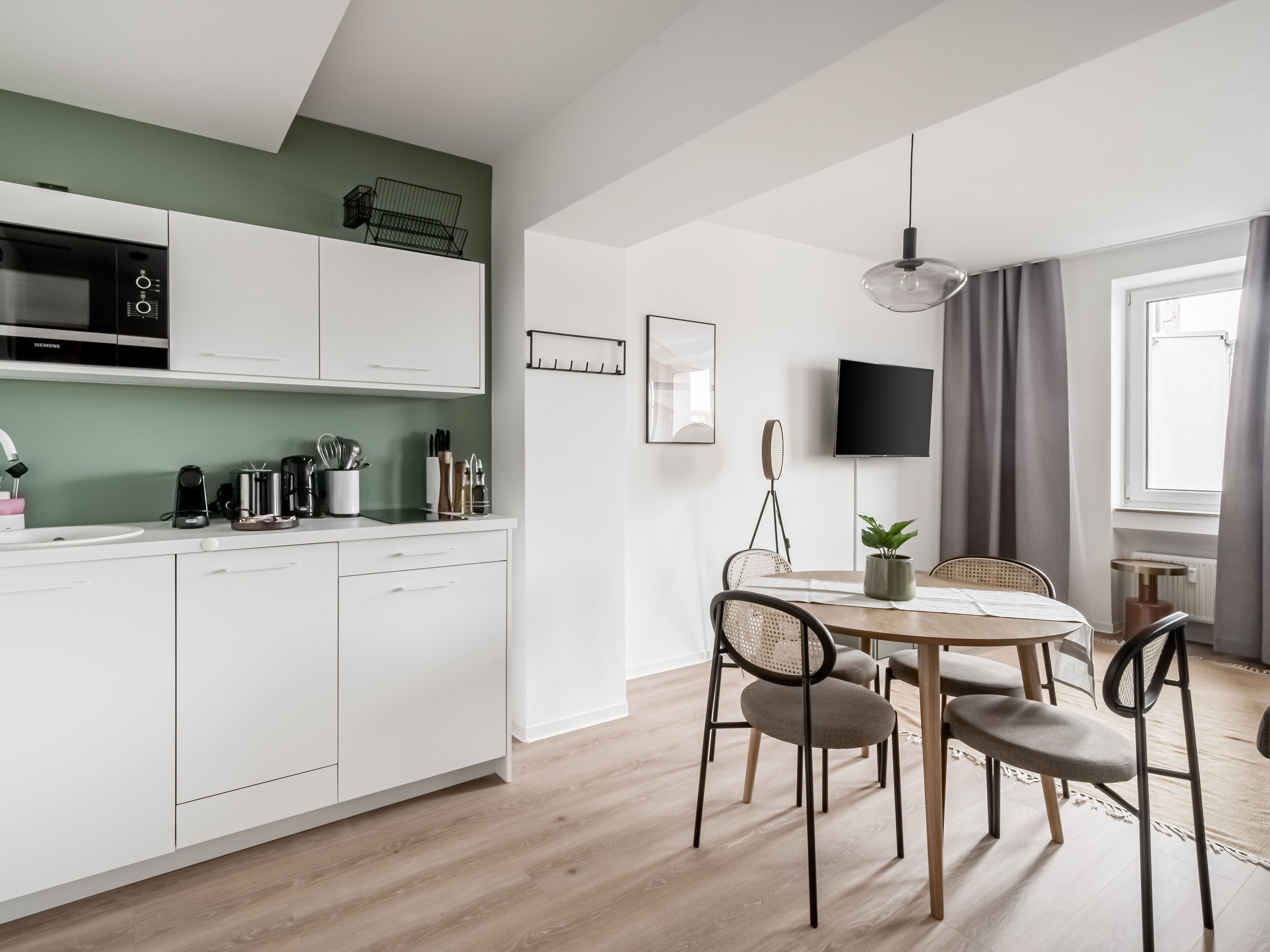 A modern kitchen with white cabinets, a microwave, and a dining area with a round table and chairs.