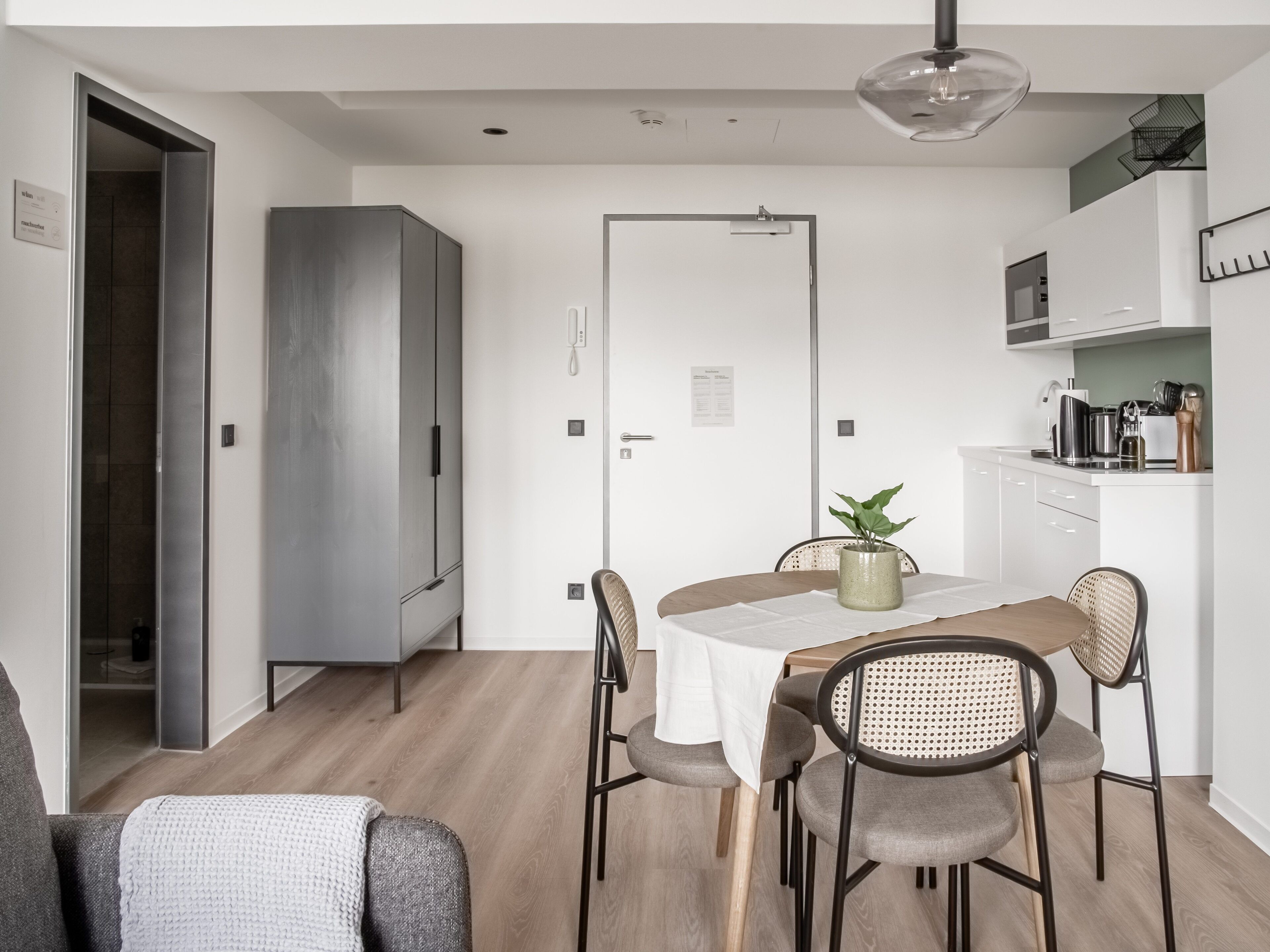 A modern kitchen with white cabinets, a dining table with a white tablecloth, and a hanging light fixture.