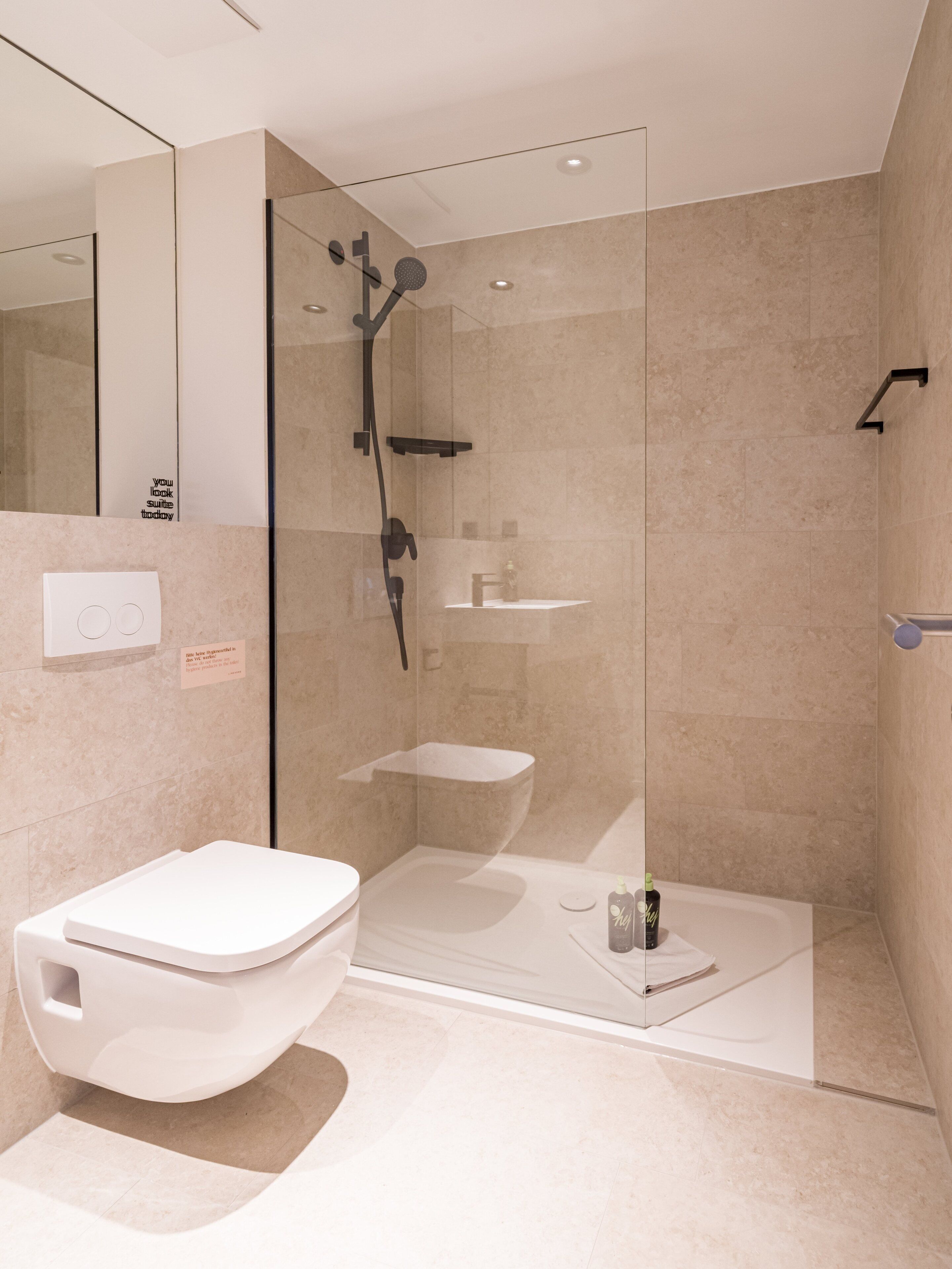 A modern bathroom with a glass-enclosed shower, a white toilet, and a small sink.