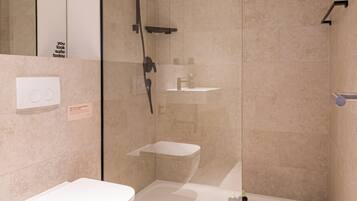 A modern bathroom with a glass-enclosed shower, a white toilet, and a small sink.
