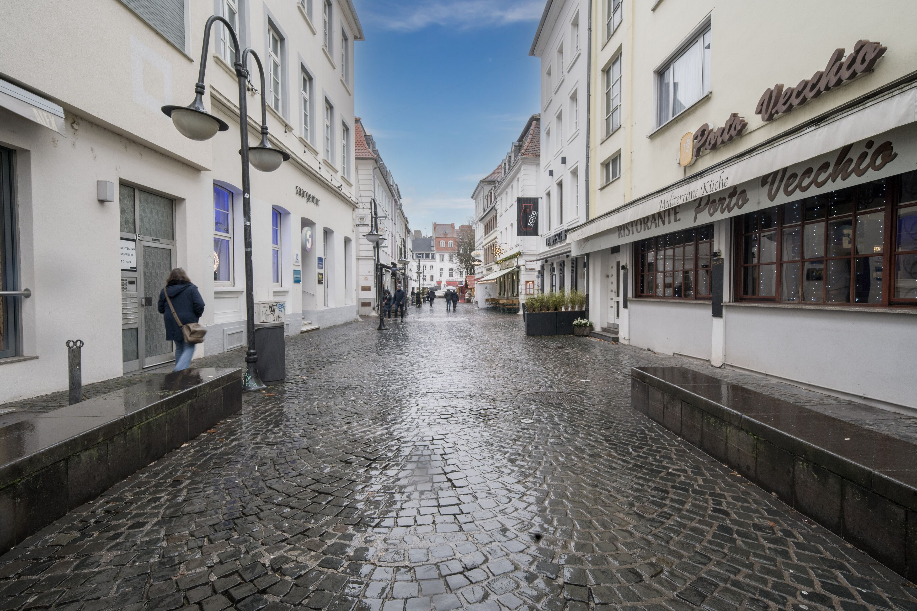 A cobblestone street with buildings on either side, including a restaurant named Porto Vecchio.