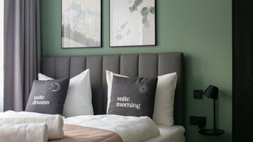 Una cama cuidadosamente arreglada con almohadas que dicen "suite dreams" y "suite morning" en una habitación con paredes verdes y un cabecero gris.
