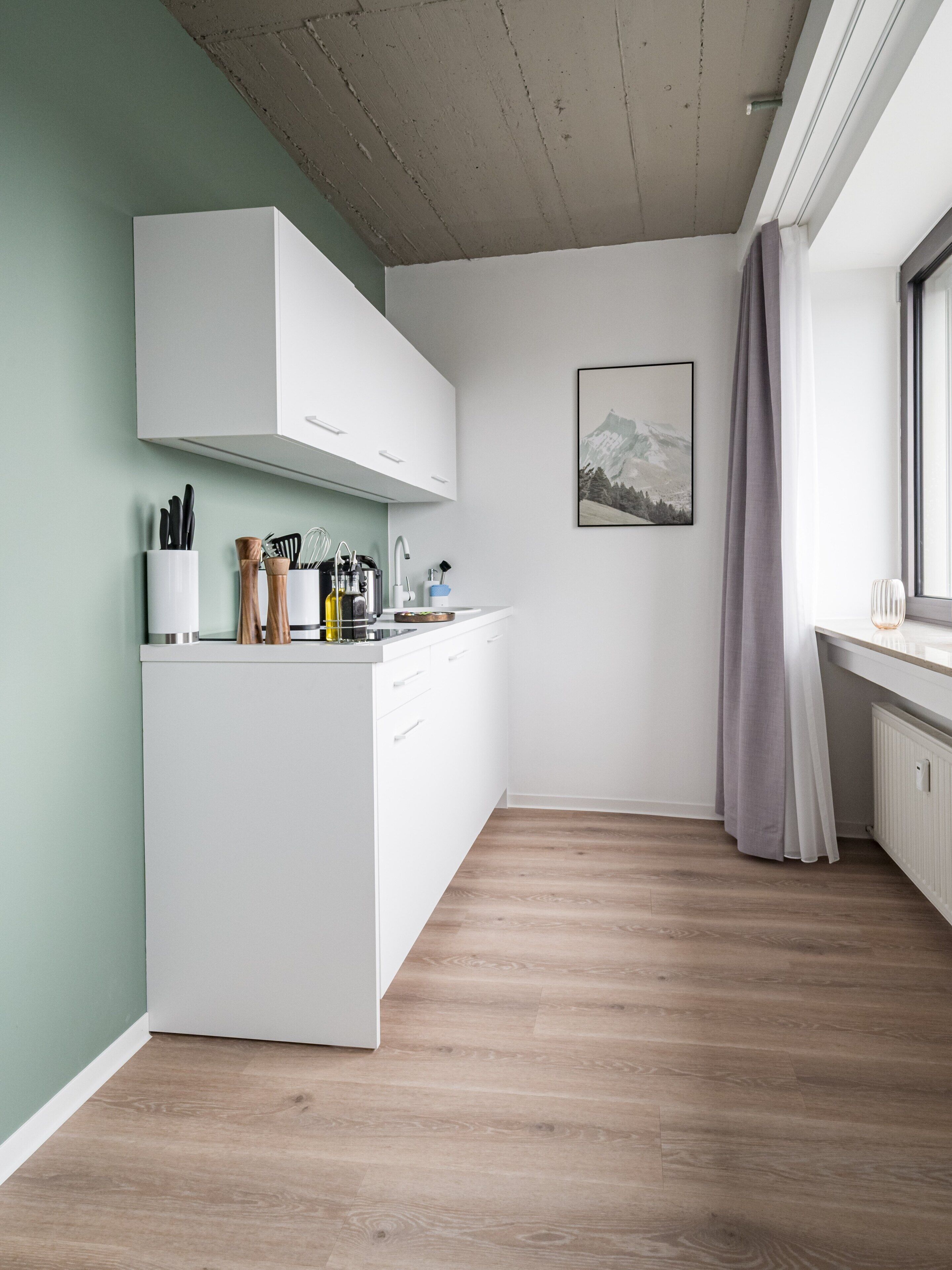 Una cocina moderna con armarios blancos, una encimera de madera y una ventana con vistas a montañas.
