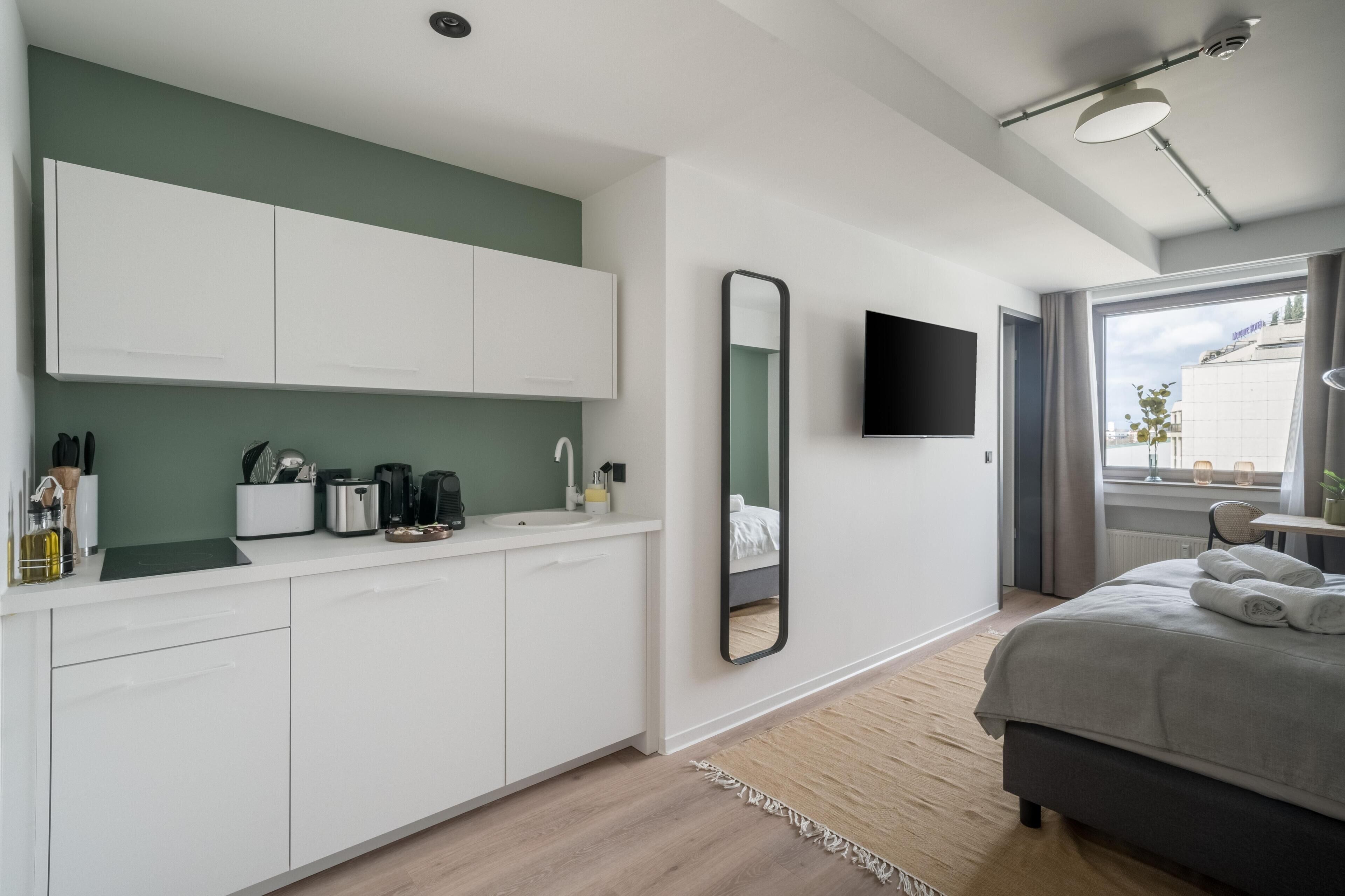 A modern bedroom with a bed, a bedside table, a mirror, and a window with curtains.