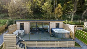 Una cabaña de madera con cerramiento de vidrio, mobiliario exterior y un jacuzzi.