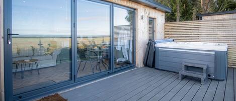 A modern outdoor deck with glass doors leading to a patio area, a hot tub, and a view of the countryside.