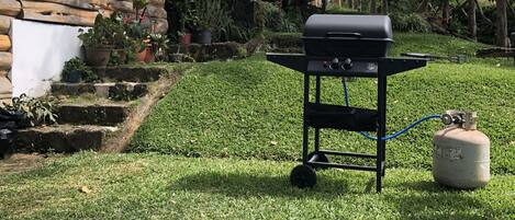 A wooden cabin with a black grill and propane tank in the yard.