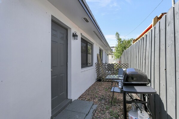 A backyard with a barbecue grill, a table, and a chair. - Spacious 1 bedroom, East Delray parking, W/D, BBQ (Delray Beach)