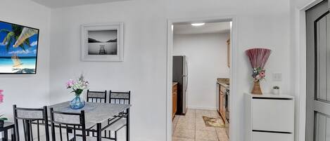 Ein Essbereich mit Tisch und Stühlen, einem Kühlschrank, und einer durchgehenden Tür erkennbaren Küche.