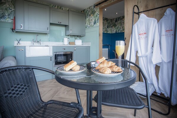 A kitchen with light blue cabinets, a dining table with chairs, croissants, and a glass of orange juice. - Rhossili Bay Secret - Cabin - Landimore (Swansea)