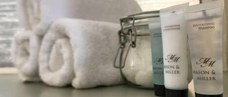 A glass jar with toiletries, including Revitalising Shampoo, next to a rolled white towel on a windowsill.