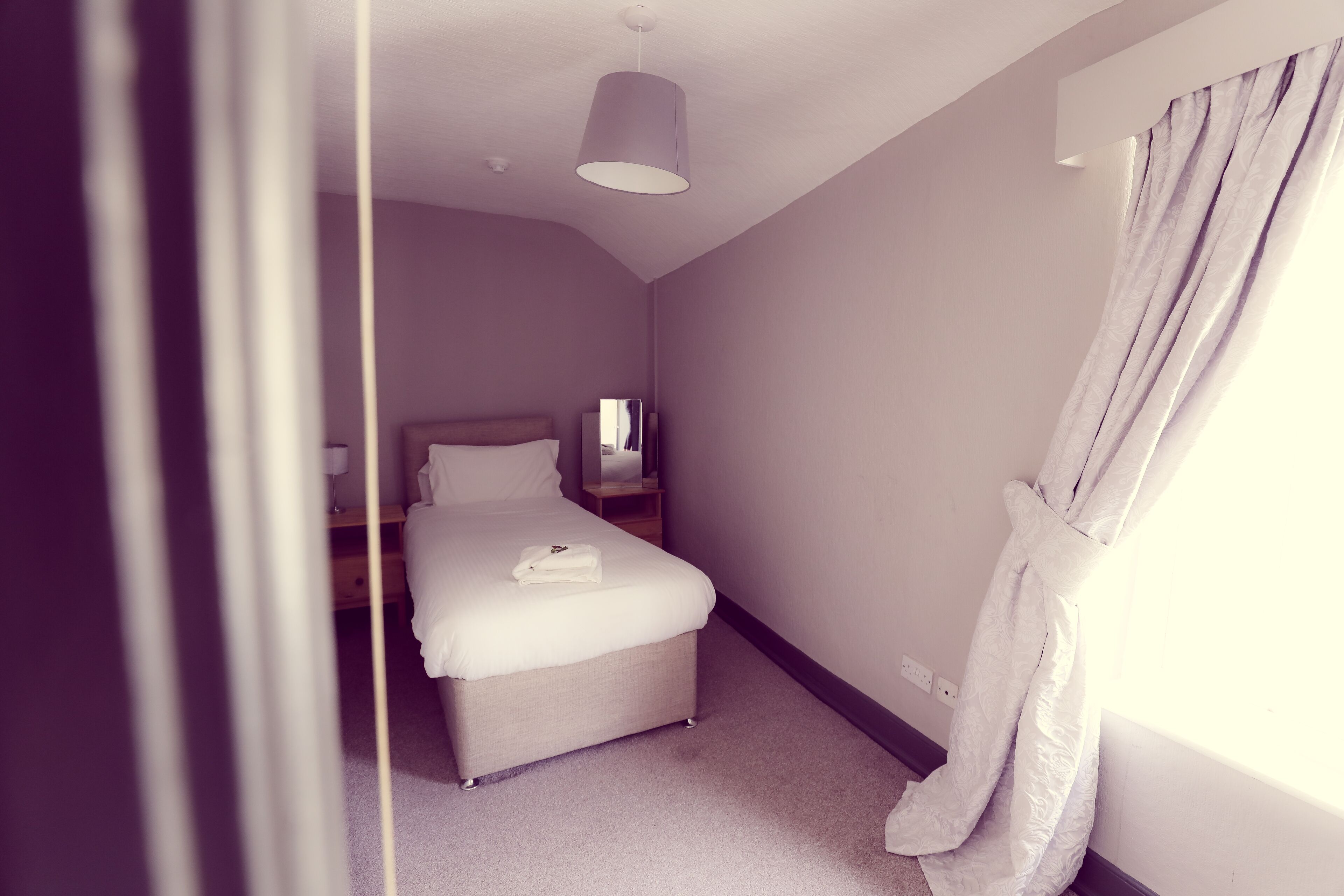 A bedroom with a bed, bedside table, and a hanging light fixture.
