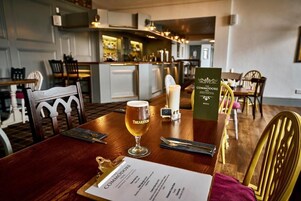 Un ambiente de restaurante con una mesa de madera, un menú, una cerveza en un vaso y una vela.