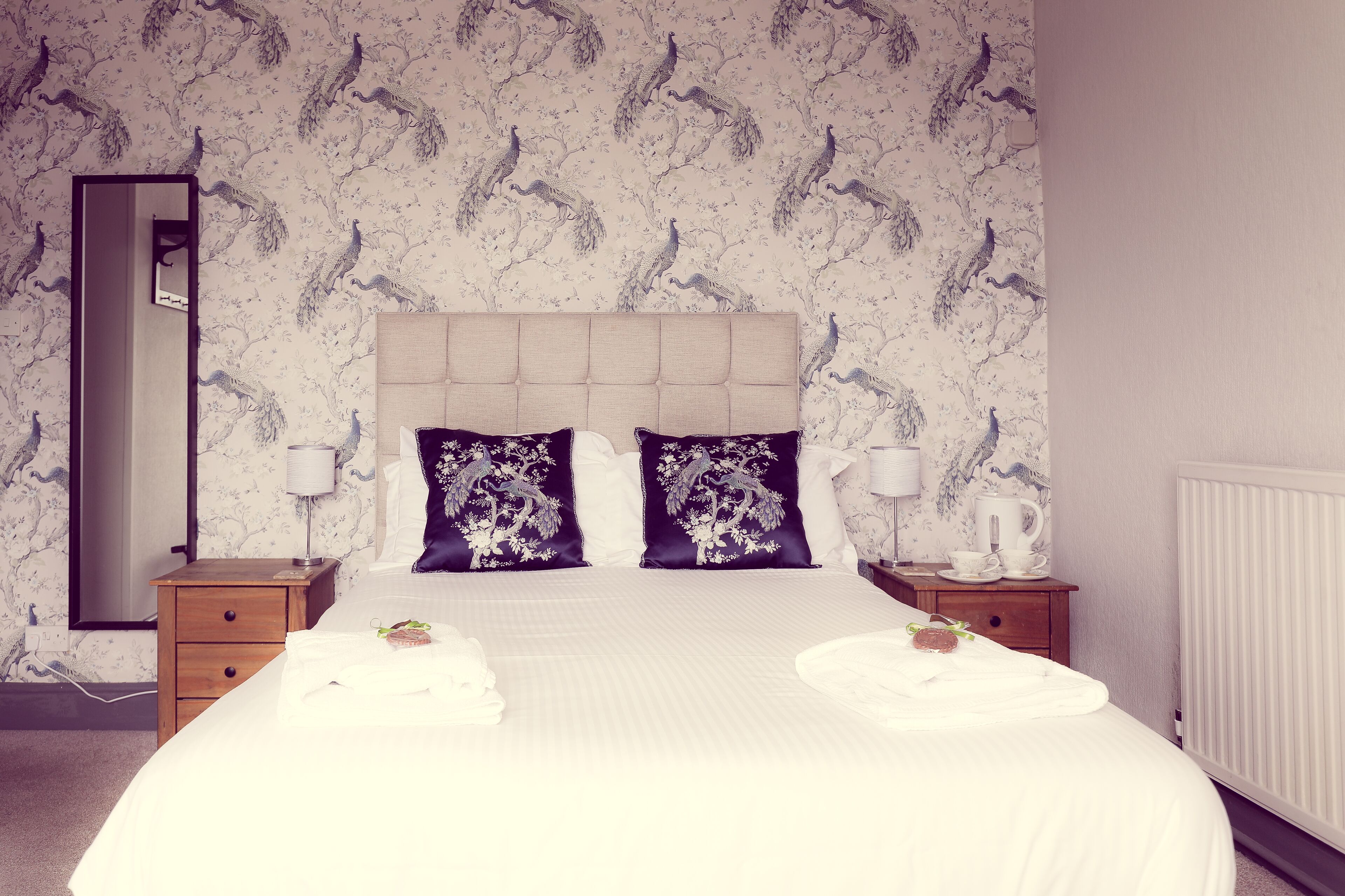 A hotel room with a large bed, two nightstands, a mirror, and a radiator.