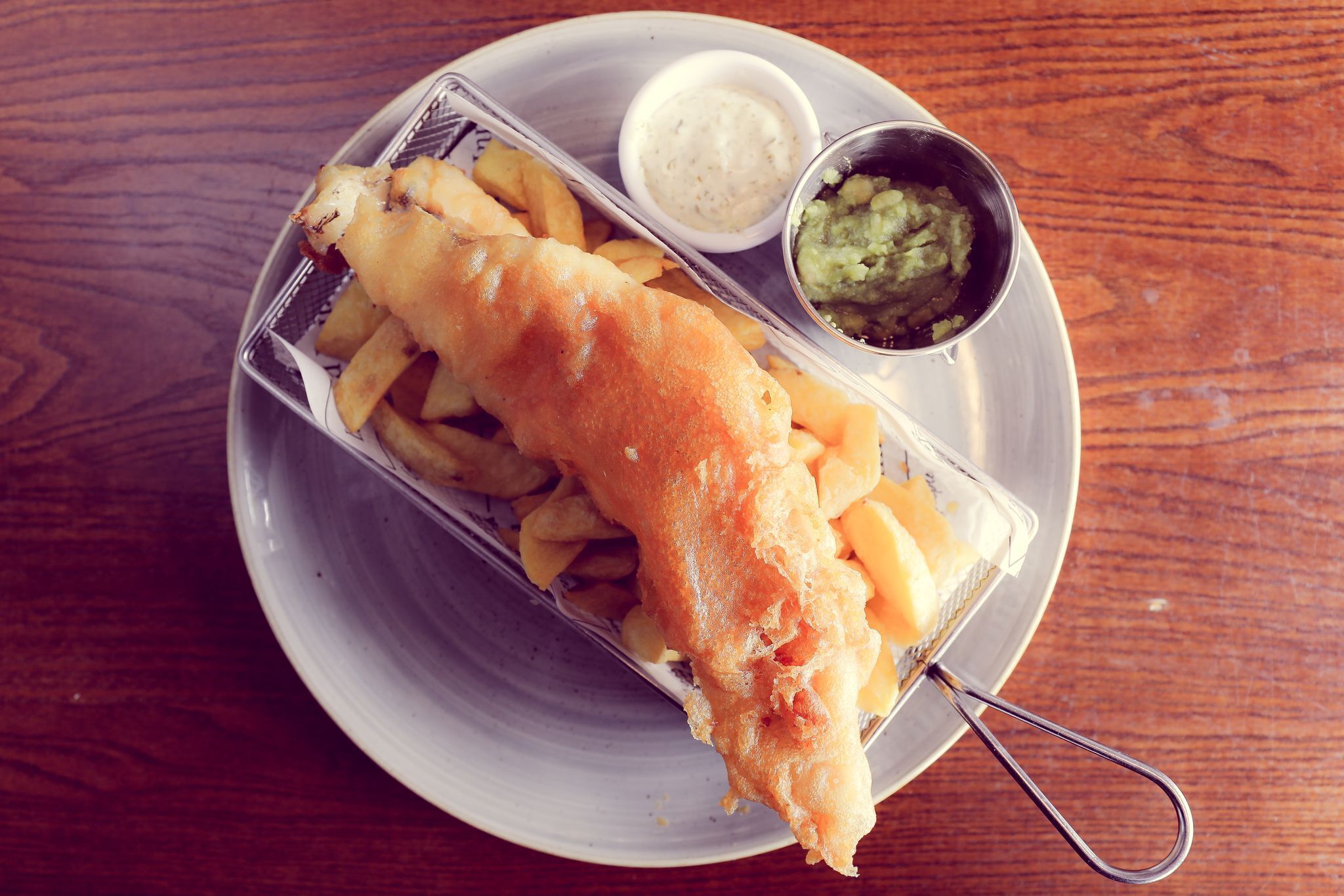A meal consisting of a fish fillet, fries, and two dipping sauces on a plate.