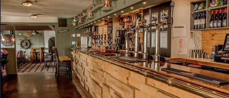 Un espace bar doté d’un long comptoir, de plusieurs robinets et d’étagères remplies de bouteilles.