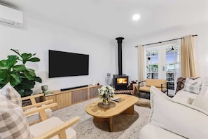Una sala de estar con chimenea, televisor de pantalla plana, una planta grande y un sofá.