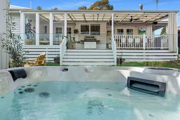 Ein Whirlpool vor einem Haus mit einer Veranda und Treppen, die zu einer Terrasse führen.