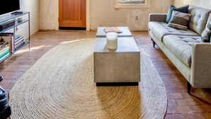 Un salon spacieux avec un haut plafond en bois, une grande fenêtre, un canapé, une table basse et un téléviseur posé sur un meuble.