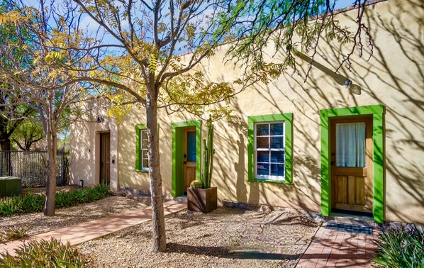 A building with green-framed windows and doors, a cactus in a planter, and a tree in the foreground. - Barrio Viejo Downtown Adobe - KING Bed + Patio + Free Parking (Tucson)