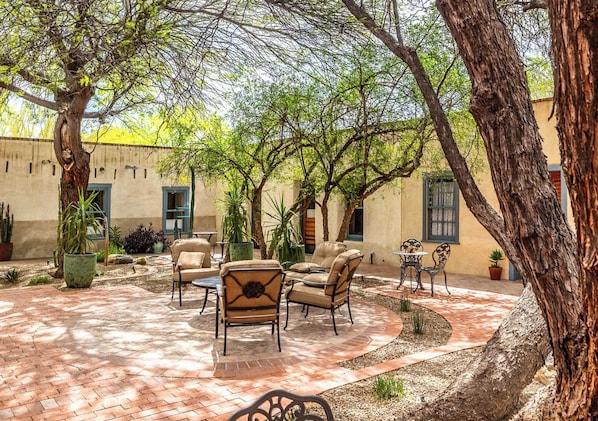 An outdoor patio with brick flooring, surrounded by trees and potted plants, featuring outdoor seating and tables. - Downtown Rustic Adobe - Newly Renovated Historic Property - KING Bed & Parking (Tucson)