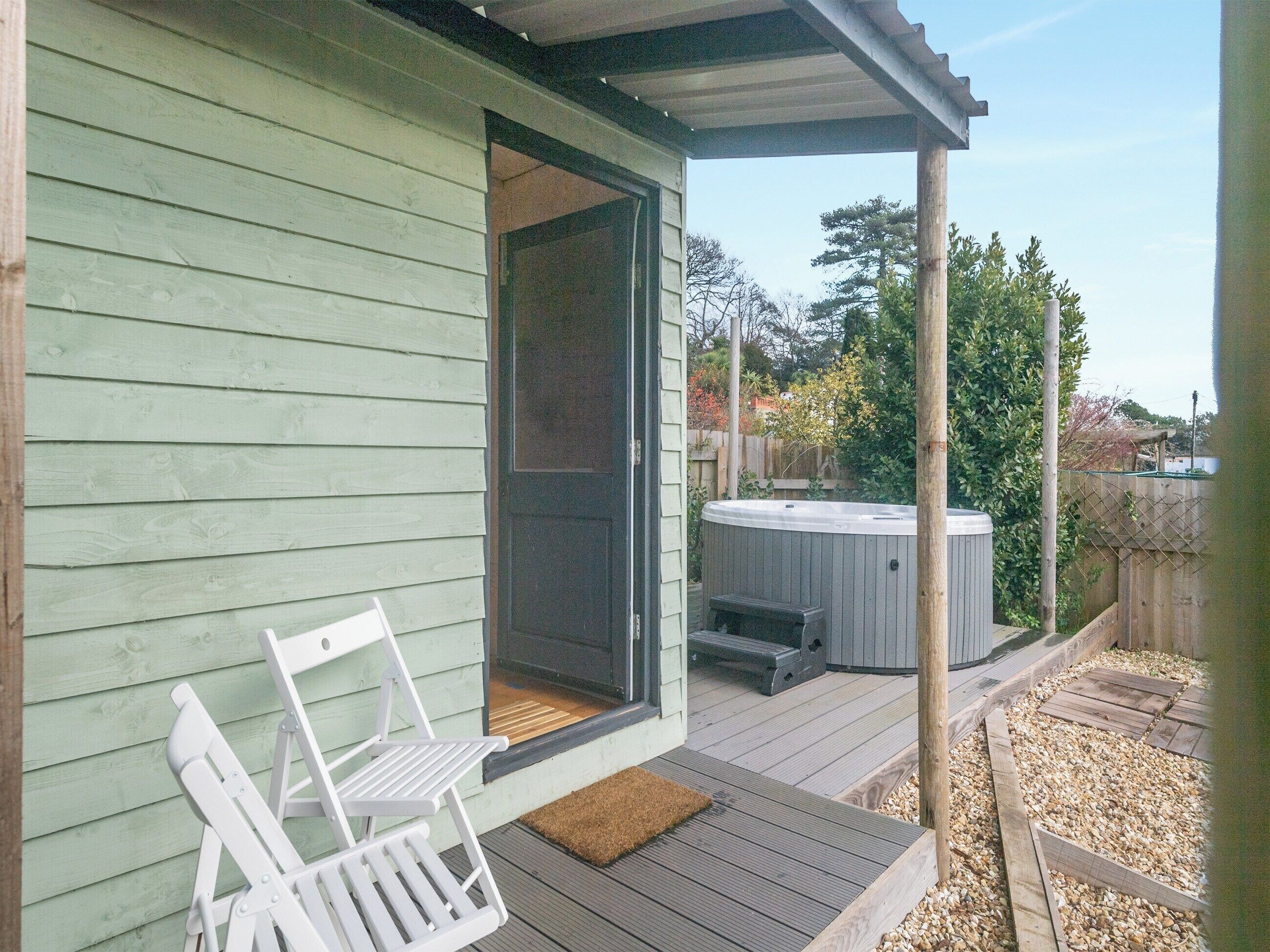 A wooden deck with a hot tub and two white chairs.