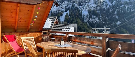 A wooden deck with a table and chairs, overlooking a snowy mountain landscape.